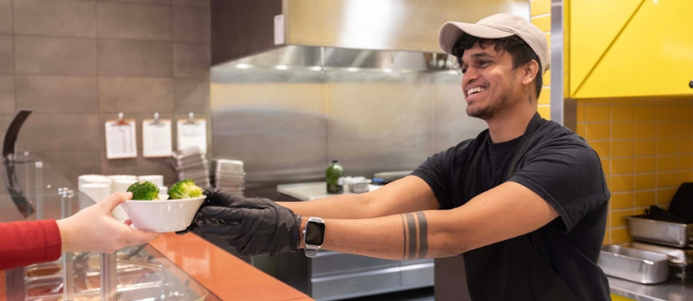 photo of smiling student employee handing plate of food across counter